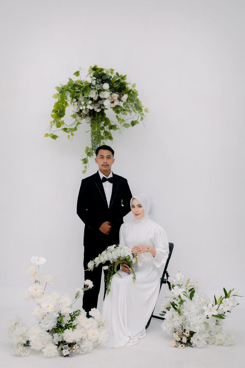 Potret formal pasangan dengan jas hitam dan gaun putih di antara bunga