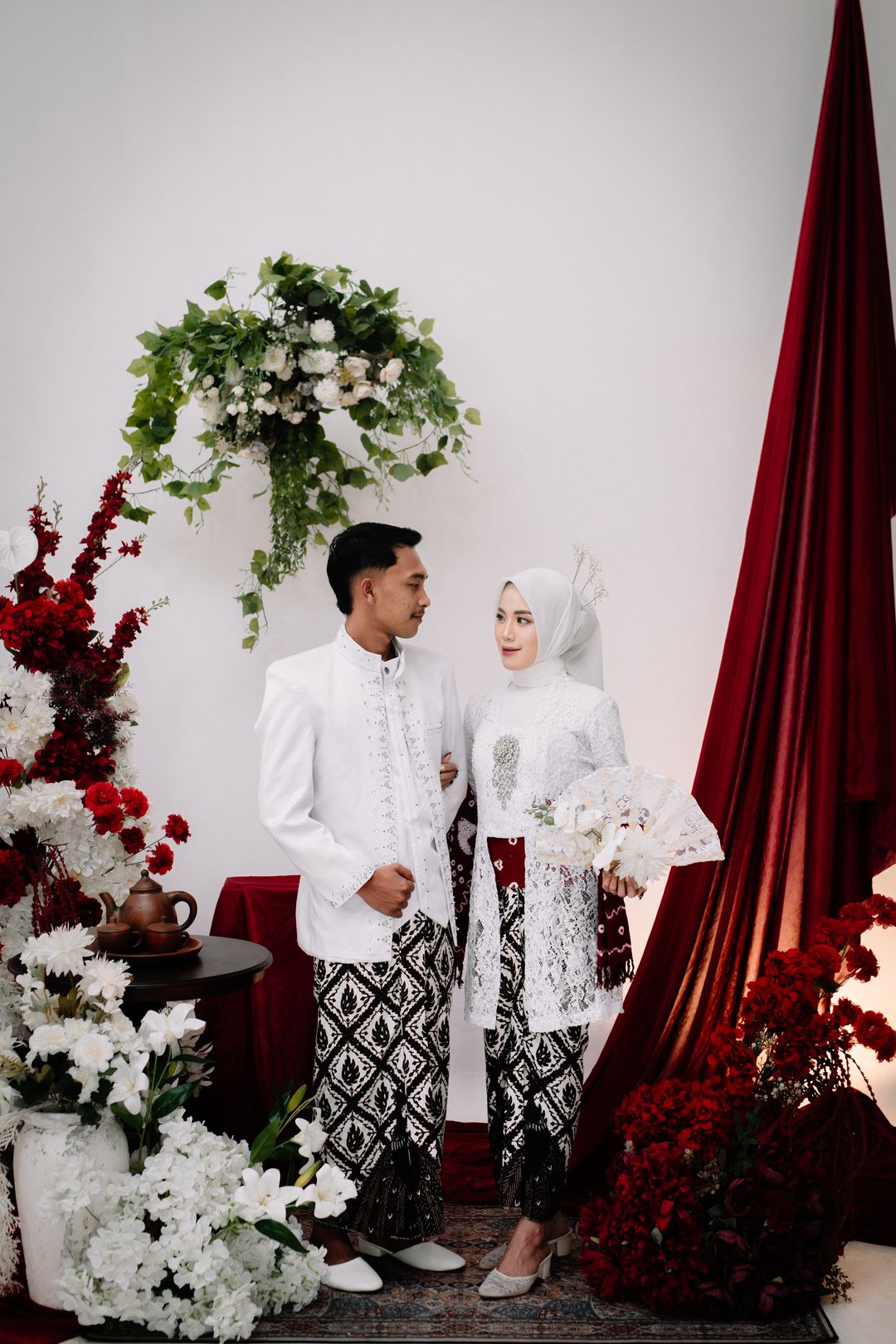 Rahardiyan dan Safrina saling menatap di antara bunga putih dan tirai burgundy